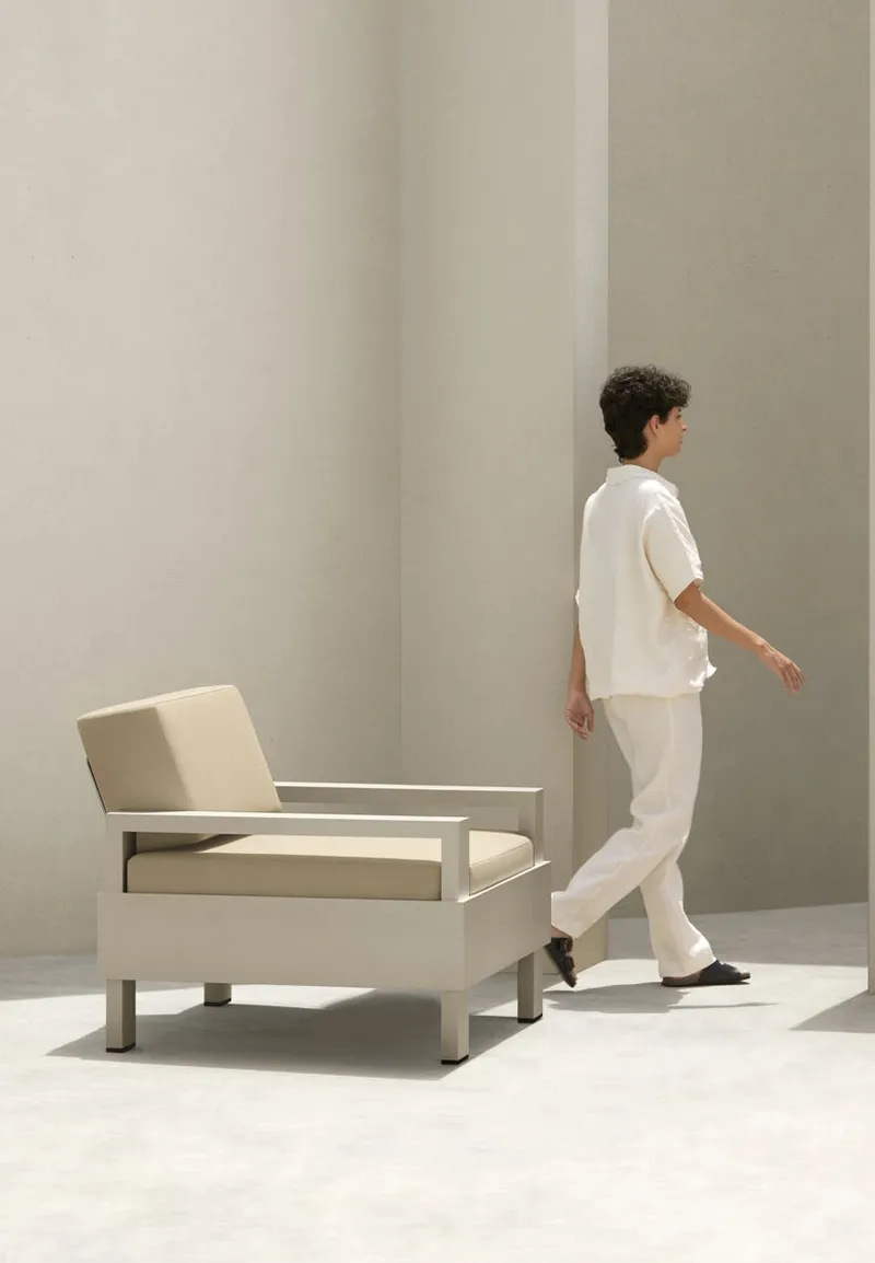 Light aluminium Hana armchair with beige cushions, a person walking past